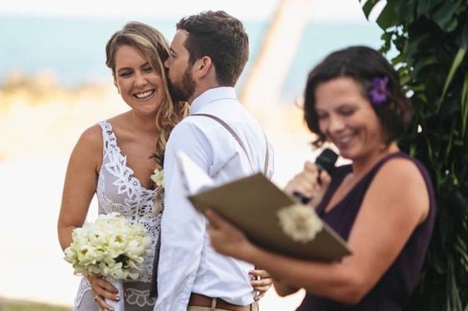 newlywed husband kissing wife in front of Cairns marriage celebrant Ali